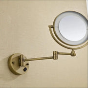 Brass wall mounted illuminated makeup mirror with adjustable arm and bronze brass wall finish for bathroom use