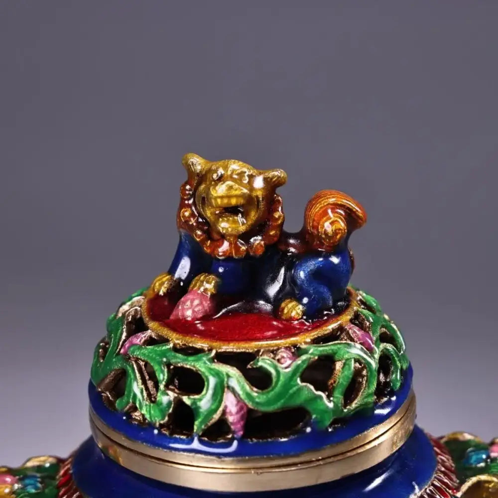 A bronze cloisonne lion incense burner with blue and gold detailing on a green and pink floral base for living room decorbites decor