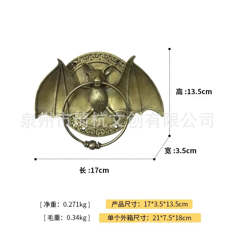 Antique brass-colored bat-shaped door knocker pendant with spread wings in a bronze dog head door knocker design