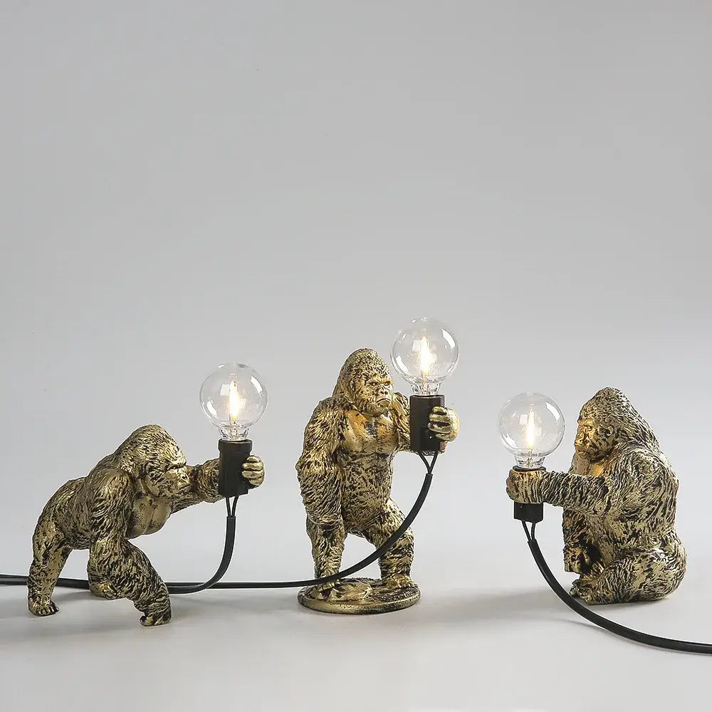 Three golden bronze king kong gorilla table lamps holding lit bulbs connected by black cords for bedroom lighting