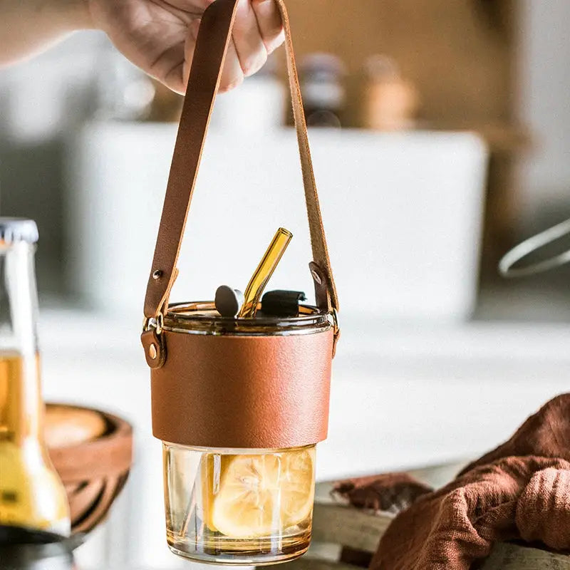 Brown leather glass coffee cup with handle featuring a transparent glass coffee cup with sliced lemons and gold straw