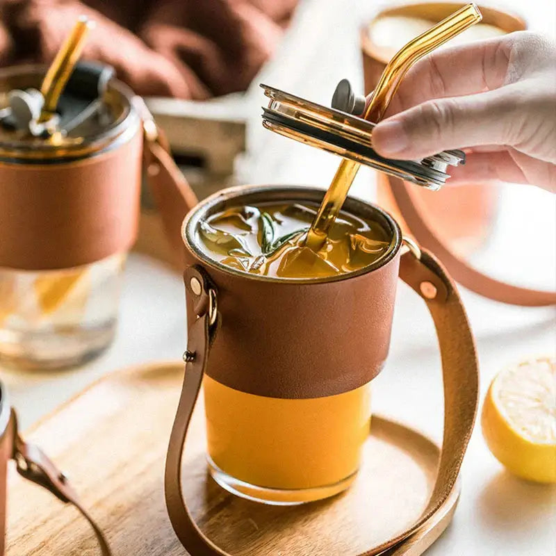 Brown leather-wrapped glass coffee cup with handle and gold-colored straw for stylish kitchen tumbler use
