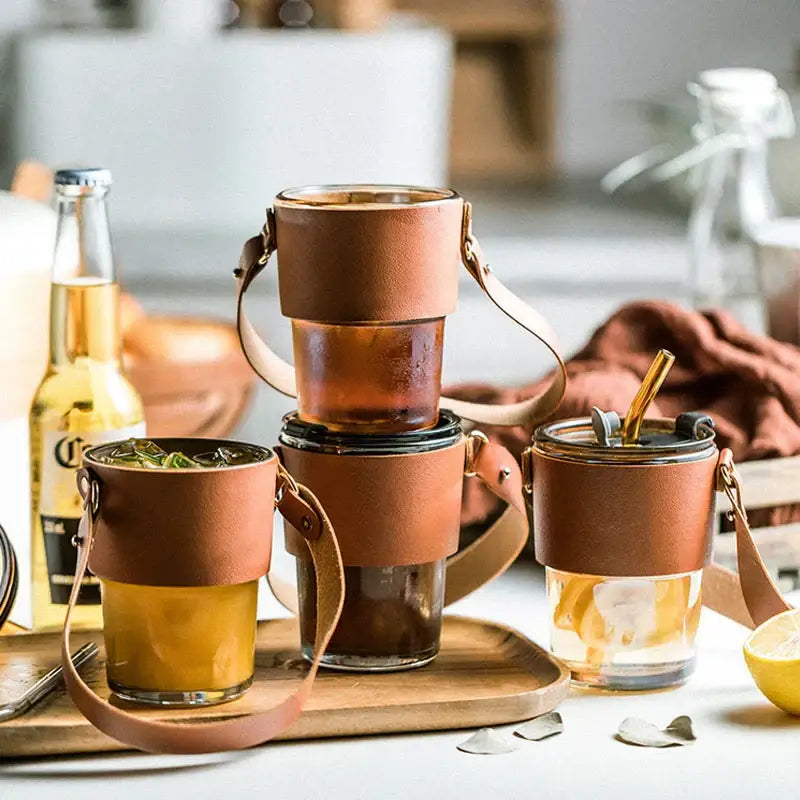 Brown leather glass coffee cup with gold straw and adjustable strap wrapped around glass tumbler
