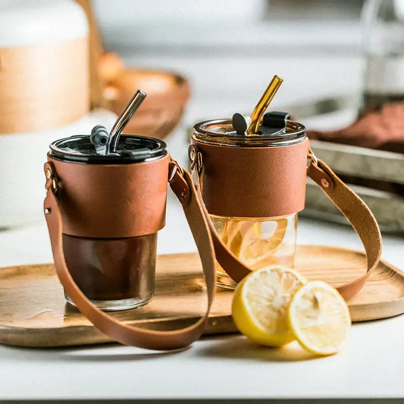 Brown leather-wrapped glass coffee cups with black lids and gold straws ideal for kitchen use and daily coffee cup use