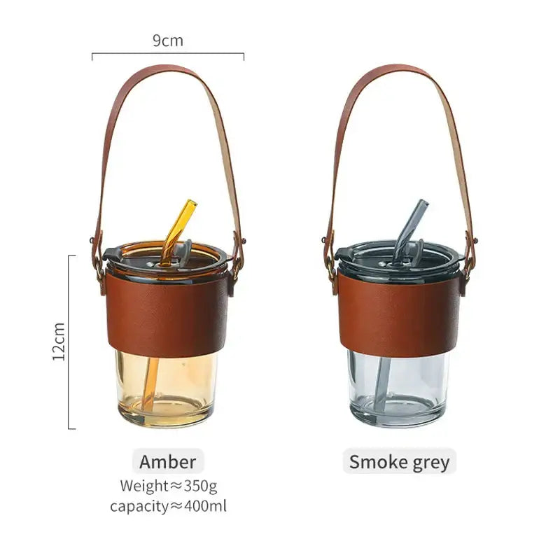 Two insulated glass coffee cups with amber and smoke grey bodies, brown leather sleeves, and gold straws for kitchen use