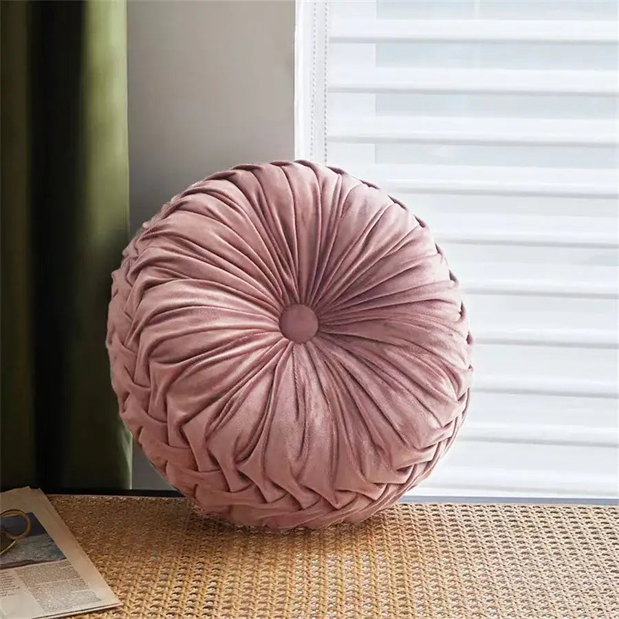 A plush dusty rose velvet round seat cushion with gathered radial design and central button for living room use