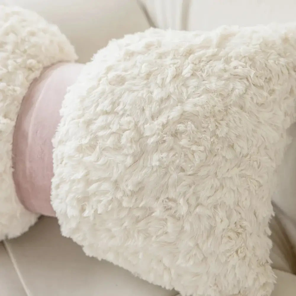 Cream-colored plush teddy bear with soft pink velvet band beside brown and white geometric embroidery plush cushion cover