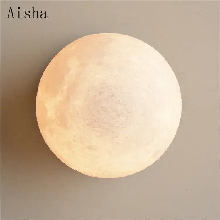 A soft warm-lit brushed brass decorbites circular planet wall lamp with a textured lunar crater surface for bedroom use