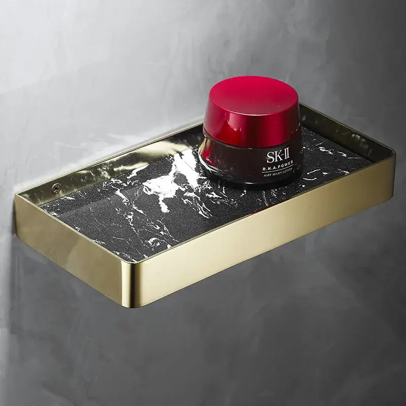Gold-framed corner shelf with black marble surface holds sk-ii rna product in decorbites brushed gold bathroom organizer