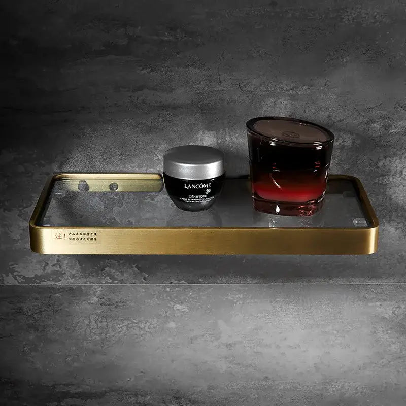 Brushed gold and black corner shelf with glass tier holding lancôme skincare and dark red gradient candle decorbites brushed gold bathroom