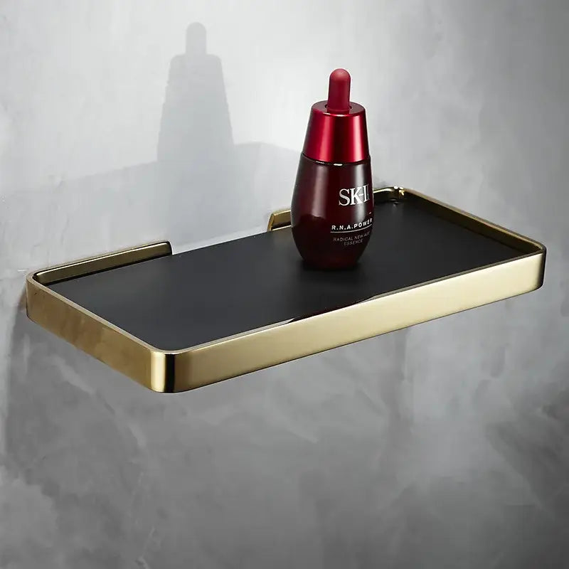 Gold-framed black rectangular corner shelf holding red sk-ii facial essence by decorbites brushed gold bathroom organizer