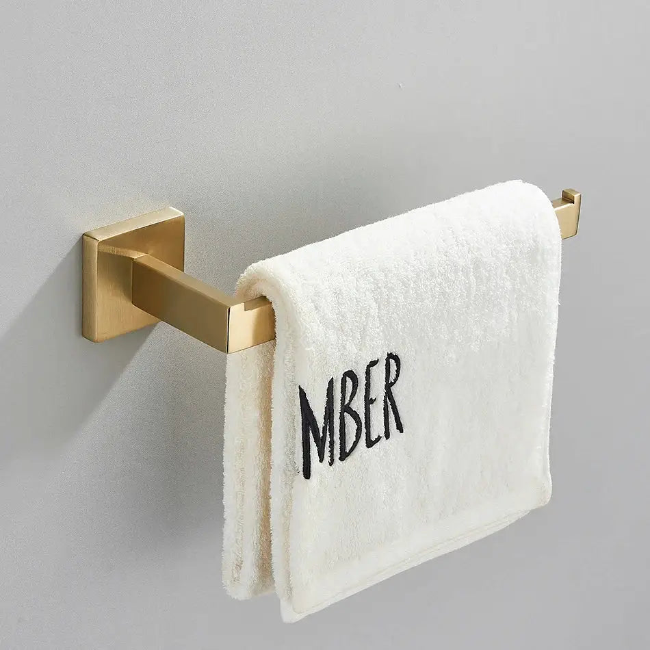 Brushed gold bathroom towel rack set with multi bar shelf and hooks holding a white terry cloth towel embroidered mber