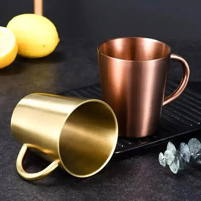 Two brushed metallic stainless steel thermal mugs with gold and copper finishes featuring integrated handles