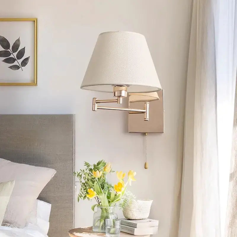 A sleek gold wall lamp with an adjustable rocker arm and tapered off-white fabric shade for living room use