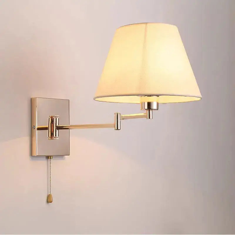 A brushed brass wall lamp with a cream fabric shade and an adjustable rocker arm for living room use