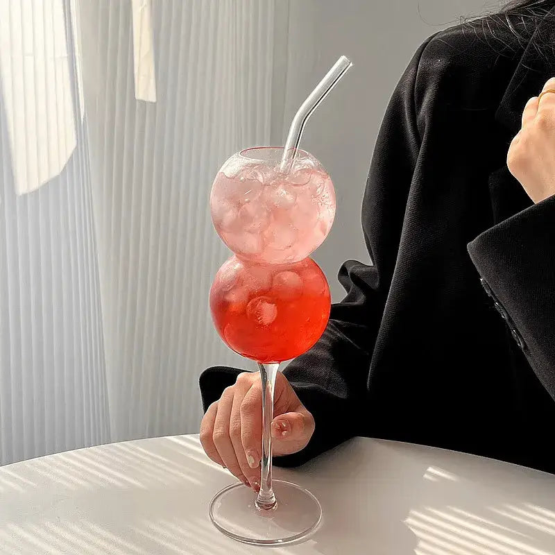 A clear double-gourd-shaped glass with pink and red drinks and ice in decorbites bubble ball stackable cocktail glass set