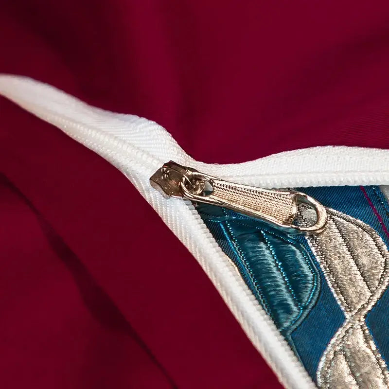 A metallic zipper with a textured pull tab on a burgundy and silver egyptian cotton embroidery bedding set