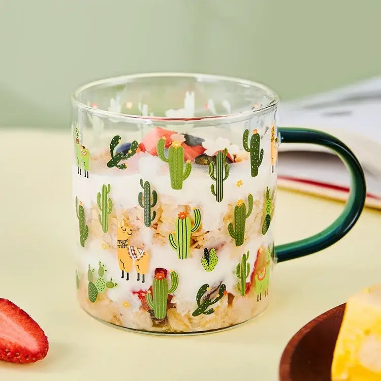 A clear glass cactus glass tea mug with a dark green handle and playful cactus and llama pattern decorbites cactus glass