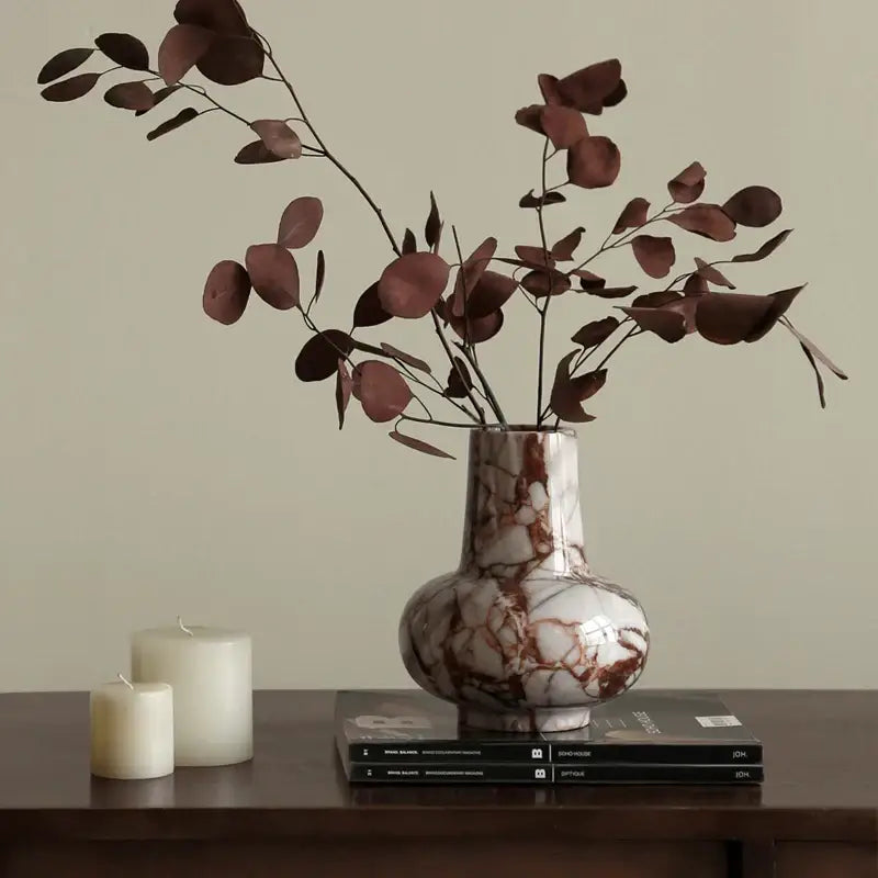 A calacatta red white and brown marble vase with rounded body holding dried eucalyptus branches for living room decor