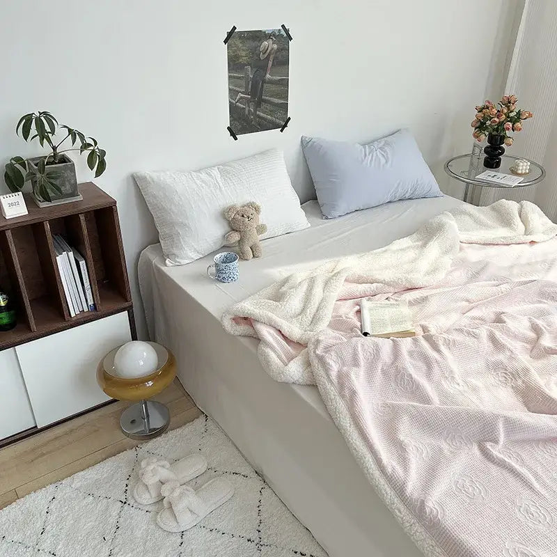 Soft pink decorbites camellia jacquard lamb wool cozy blanket with fluffy white border draped over bed