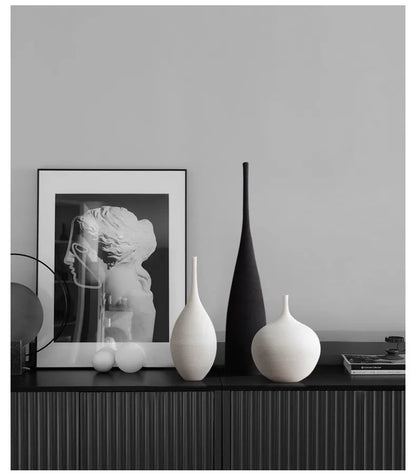 A sleek matte black ceramic CAPIRON zen vase with tall slender neck stands beside two white vases on dark console table