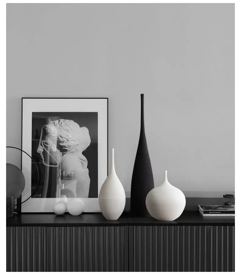 A sleek matte black ceramic CAPIRON zen vase with tall slender neck stands beside two white vases on dark console table