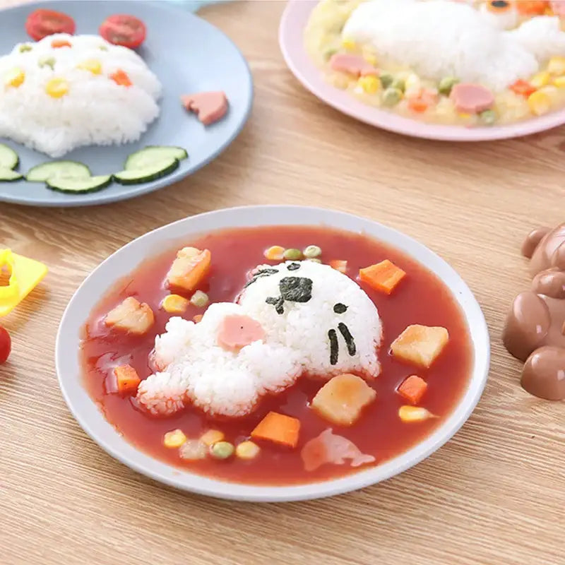 A cartoon animal sushi mold set featuring a white rice cat dish in red tomato sauce with vegetable garnishes using a sushi mold