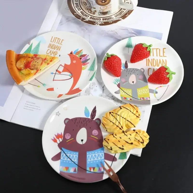 Three white ceramic bone snack plates with colorful cartoon animal designs and little indian camp text snack plate set decorbites bone snack