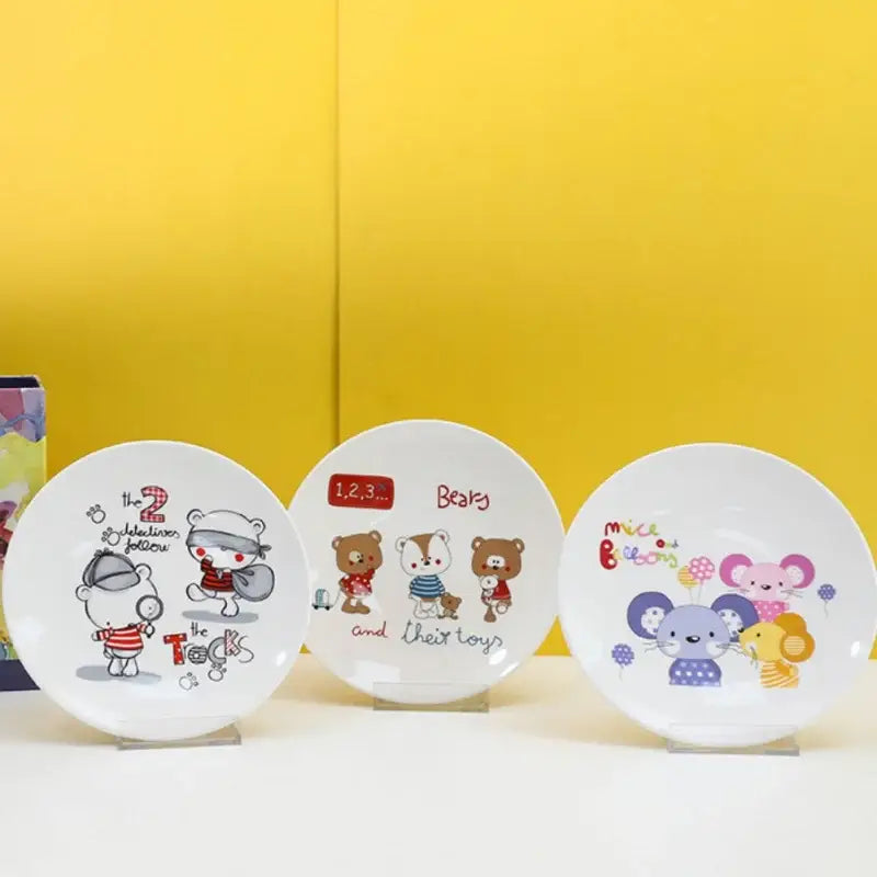 Three white ceramic bone snack plates with colorful cartoon animal and child illustrations in a decorbites snack plate set
