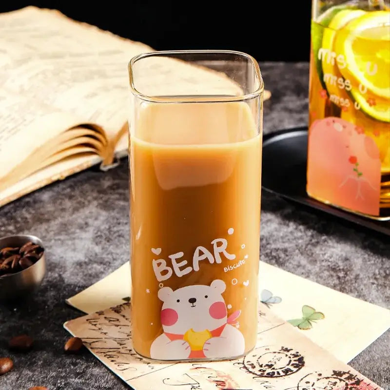 A clear glass coffee mug with a colorful cartoon bear pattern filled with an amber beverage
