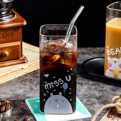 A tall clear glass coffee mug with iced dark soda and a gray cartoon bear pattern with miss u text