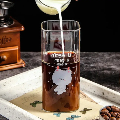 A clear glass coffee mug with a white cartoon bear design and miss u text filled with dark coffee liquid