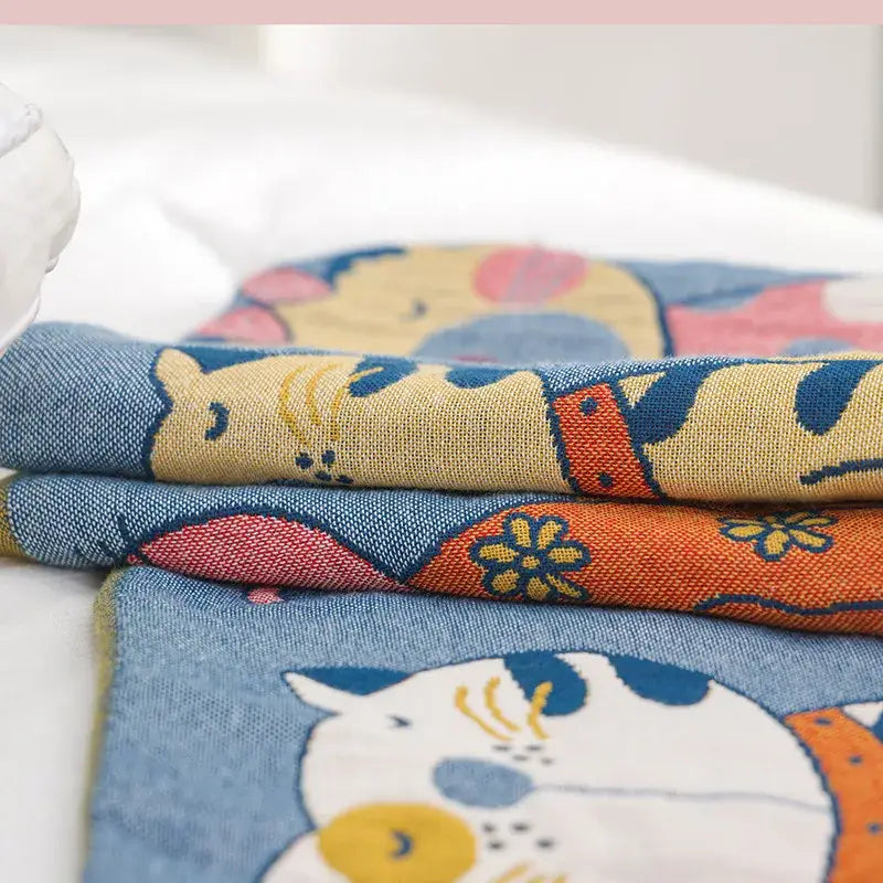 Stacked fabric pieces of decorbites cartoon boho bedspread featuring pastel cartoon cat designs on woven cotton material