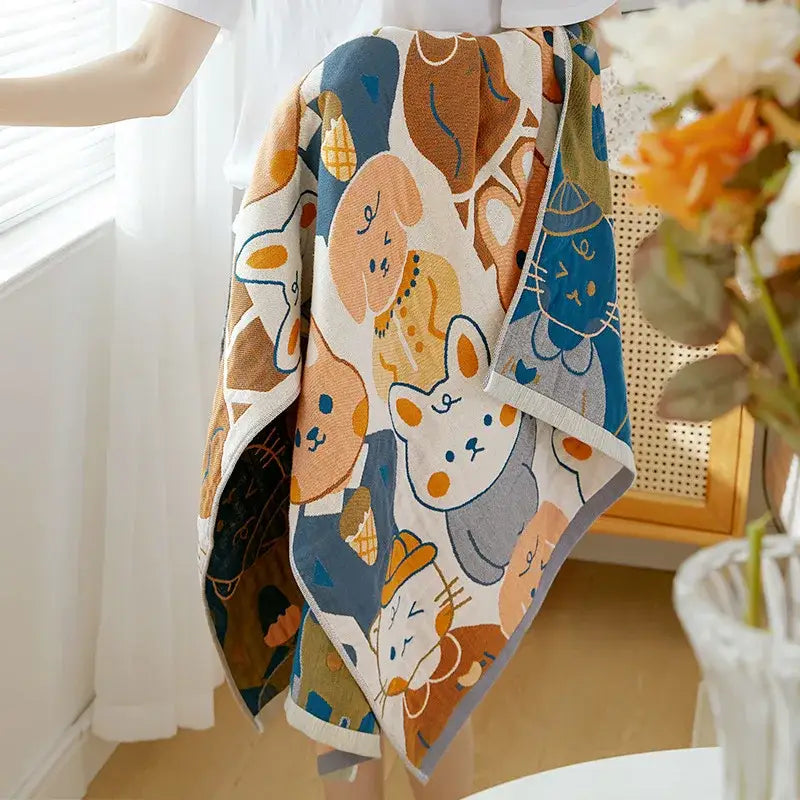 A cream-colored decorbites cotton gauze bath towel with playful cartoon cats and dogs in blue orange and gray