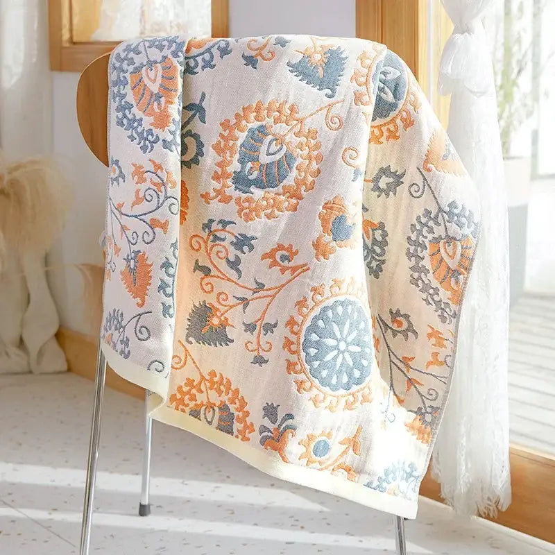 A soft cream-colored decorbites cotton gauze bath towel with embroidered floral and circular patterns in orange blue and gray
