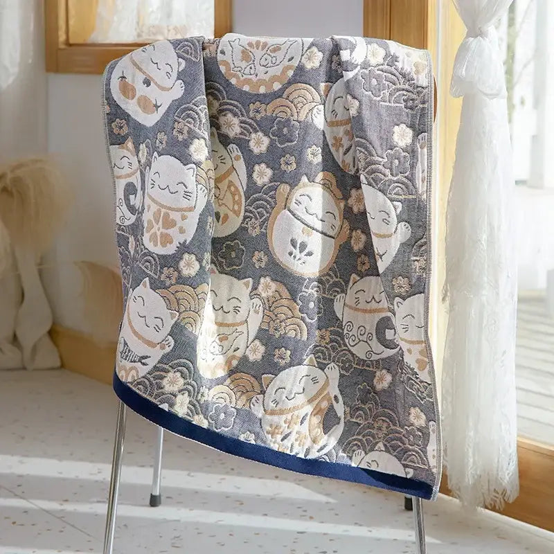 A soft gray decorbites cotton gauze bath towel with lucky cat designs and navy blue border for bathroom use
