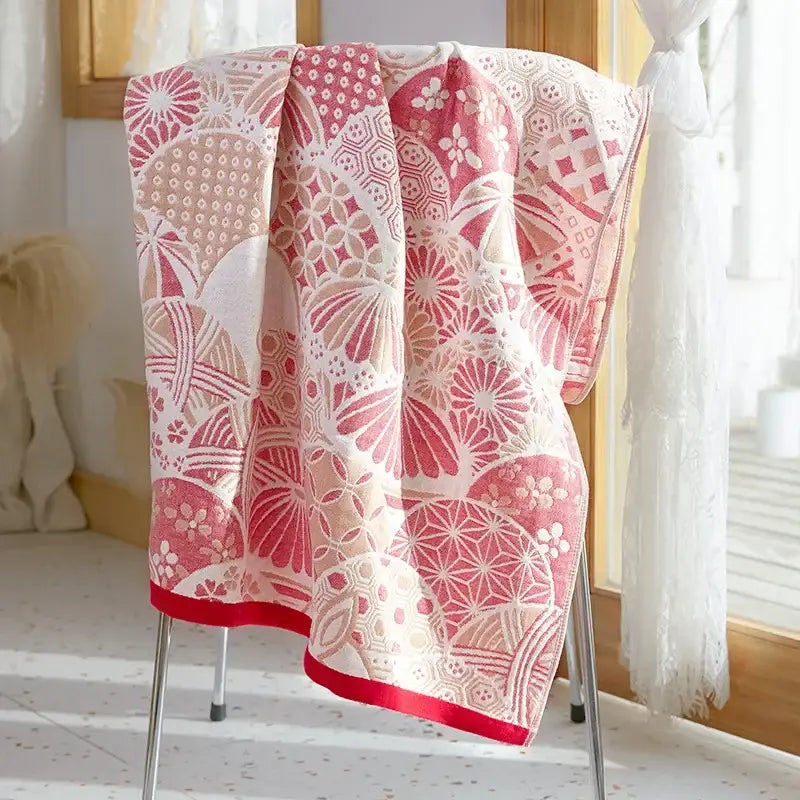 A soft pink and white decorbites cotton gauze bath towel with geometric floral patterns and a bold red border for bathroom use