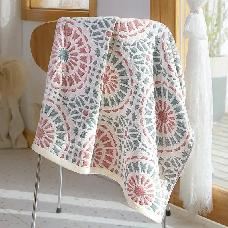 A soft white cotton gauze bath towel with pink and gray floral motifs draped over a wooden chair back decorbites cotton gauze bath towel