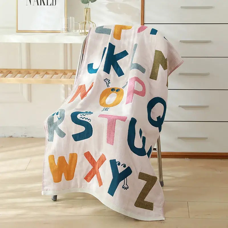 A soft off-white decorbites cotton gauze bath towel with colorful playful alphabet letters for bedroom and nursery use