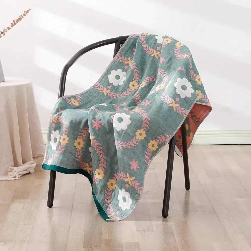 A soft teal decorbites cotton gauze bath towel with floral pattern draped over a black chair for bedroom and nursery