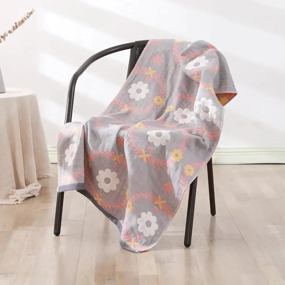 A soft gray cotton gauze bath towel with delicate floral pattern draped over a chair for bedroom and nursery use