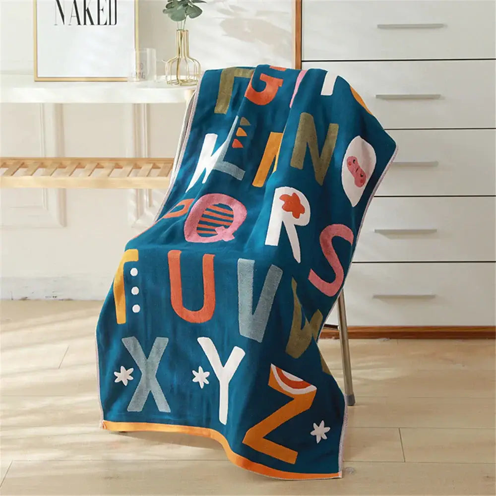 A vibrant teal bath towel with multicolored alphabet design made from decorbites cotton gauze, ideal for nursery decor