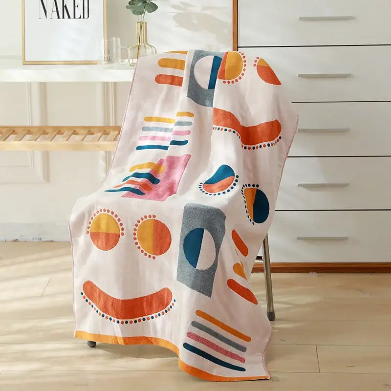 A soft off-white decorbites cotton gauze bath towel with bold orange pink blue and gray shapes for bedroom and nursery