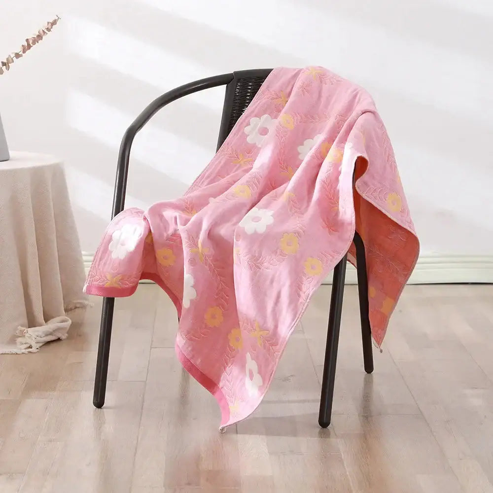A soft pink decorbites cotton gauze bath towel with white and yellow flowers draped over a black chair for bedroom and nursery decor