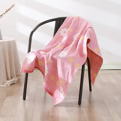 A soft pink decorbites cotton gauze bath towel with white and yellow flowers draped over a black chair for bedroom and nursery decor