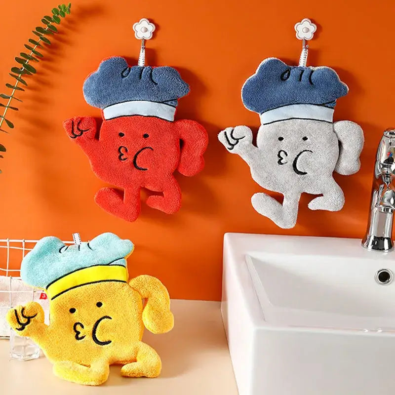 Three colorful microfiber hand towels in red yellow and gray with chef designs hang on hooks against an orange wall