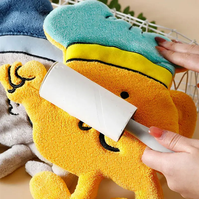 White plastic lint roller used on yellow plush character of cartoon chef microfiber hand towel with kitchen wall hooks