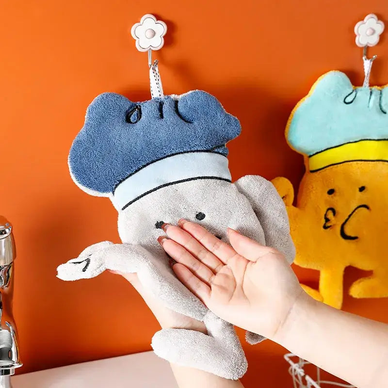 Blue and gray plush chef-themed microfiber hand towel with embroidered face hanging from flower-shaped kitchen wall hook