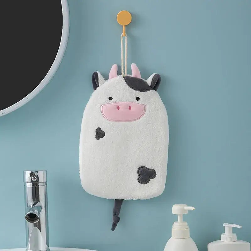 A plush white cow-shaped bath sponge with black spots and pink nose hanging from a yellow hook in decorbites cartoon embroidery hanging hand towel design