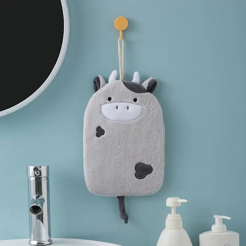 Gray plush cow-shaped bath sponge with black spots and white snout hanging from yellow hook decorbites cartoon embroidery hand towel